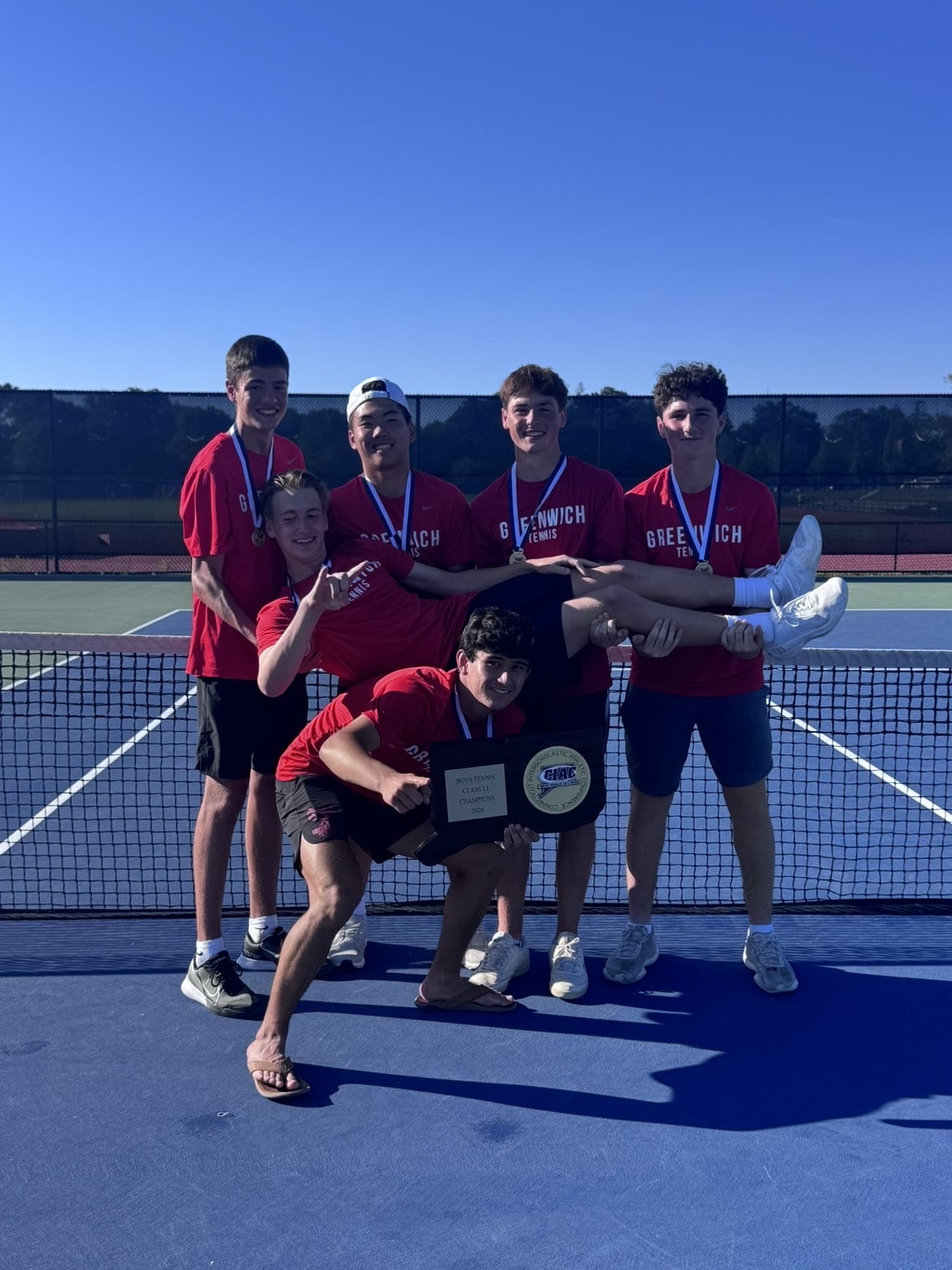 The Greenwich varsity tennis team celebrating on court with their 2026 CIAC Class LL Champion plaque. The 6NUP team members are highlighted.